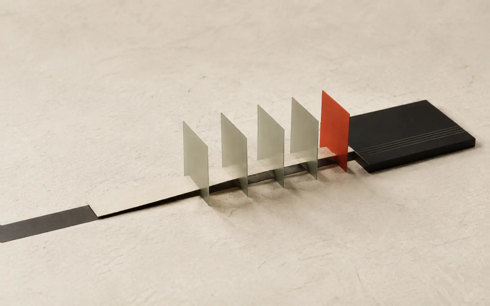 A paper strip runs through four translucent sage gates and one red gate onto a dark plate scored with fine lines.