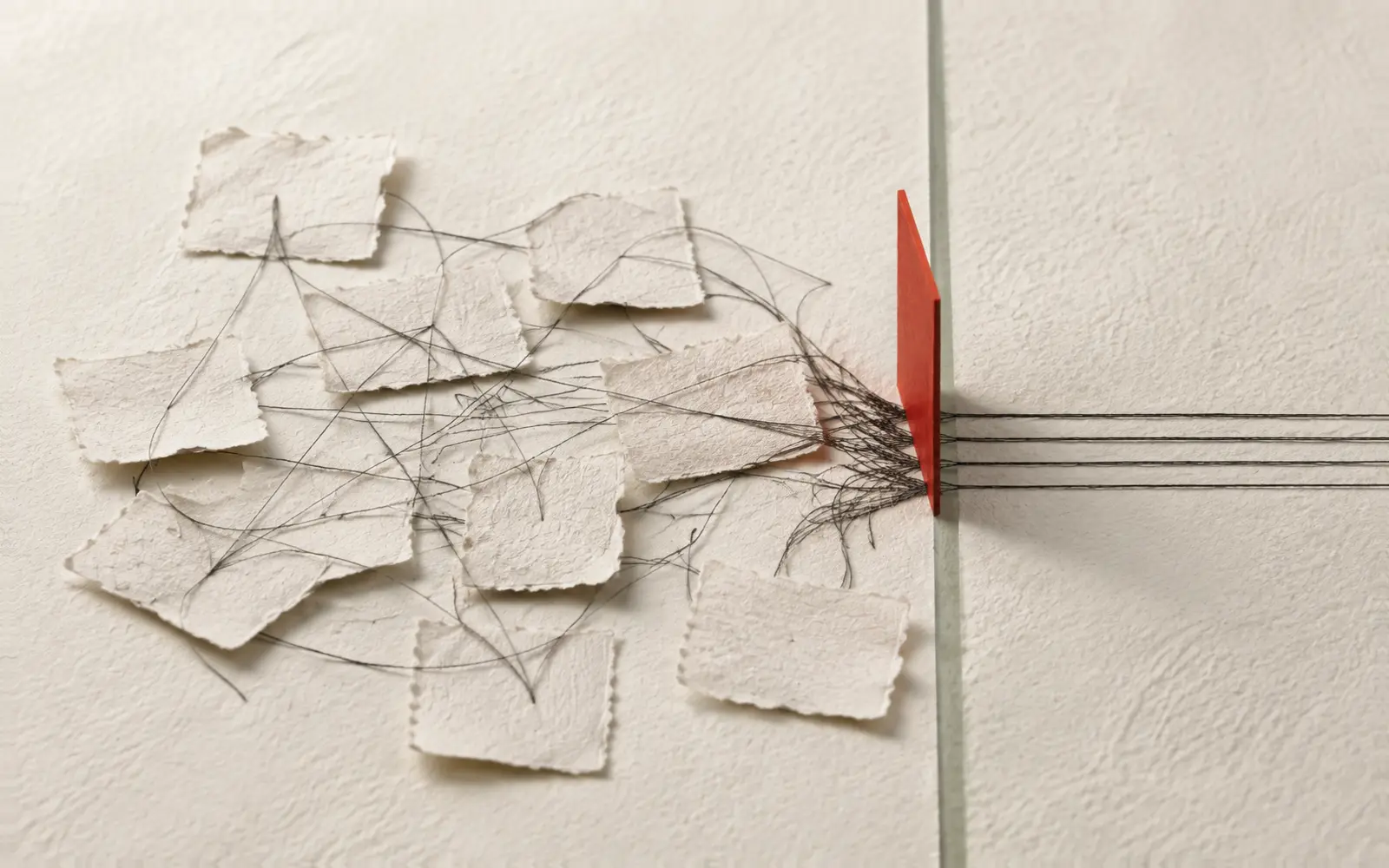 Many small sheets of paper joined by tangled thread pass one red plane and continue as a few straight parallel lines.