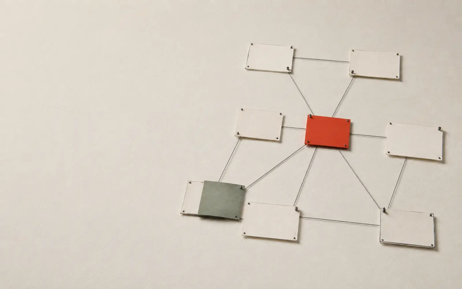 Paper index cards pinned in a network and joined by thread; one card is red, one is sage green.